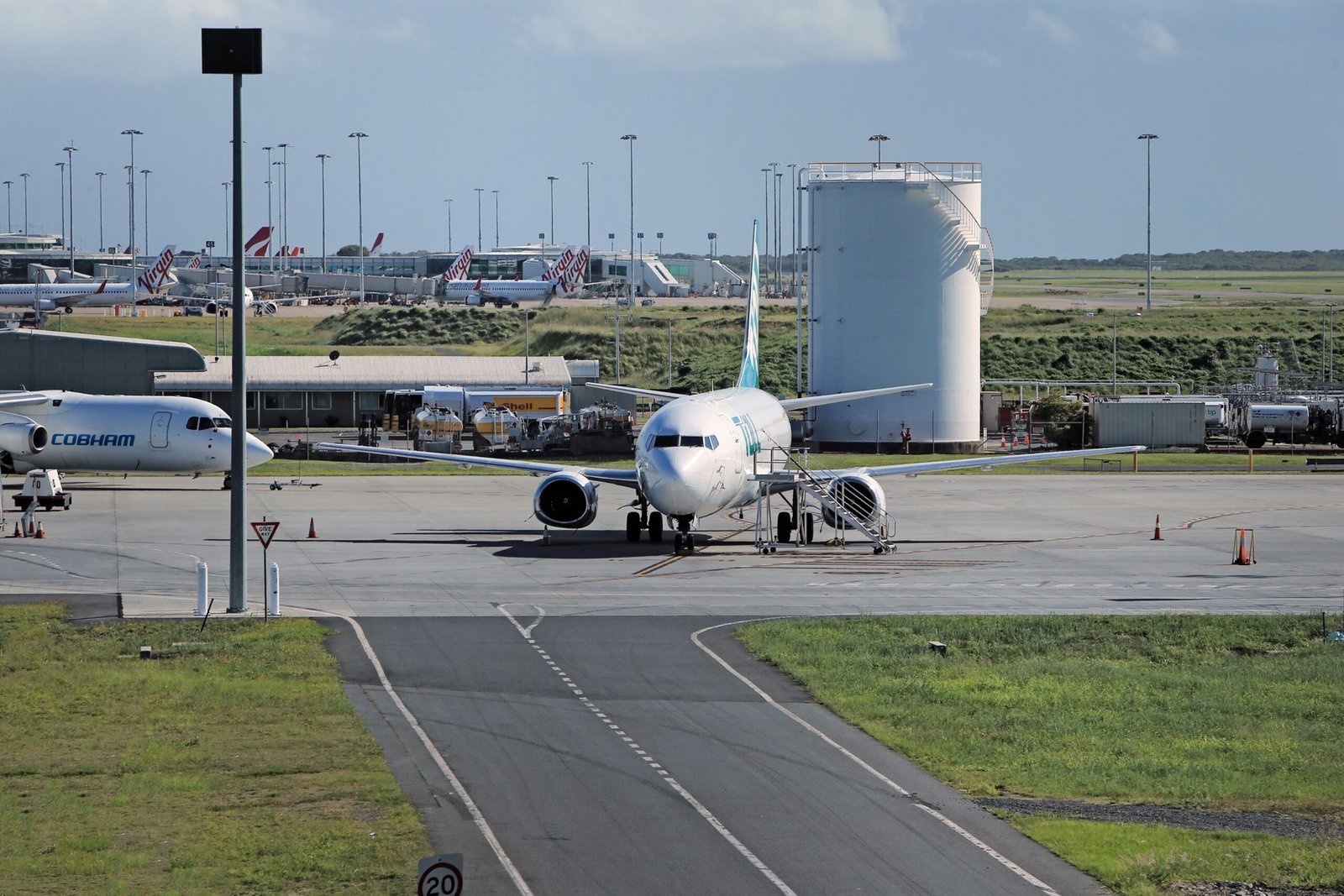 A bustling airport taxiway with commercial airliners and service vehicles under a clear sky.