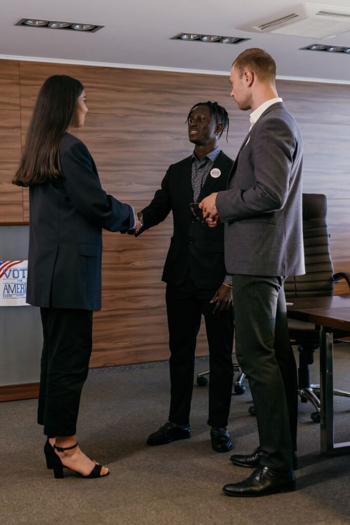 Network Three professionals in a conference room handshake during a business meeting.